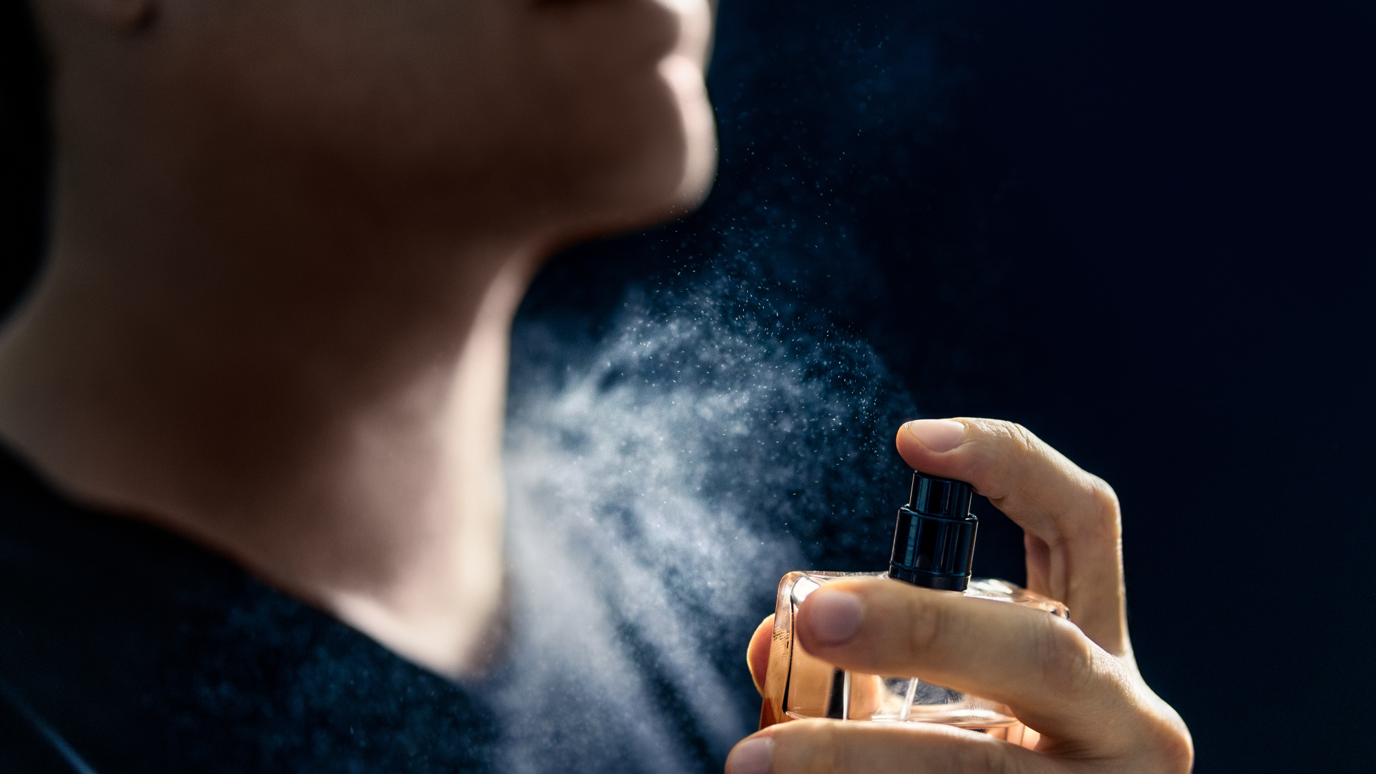 Close-up of a person spraying perfume on their neck.
